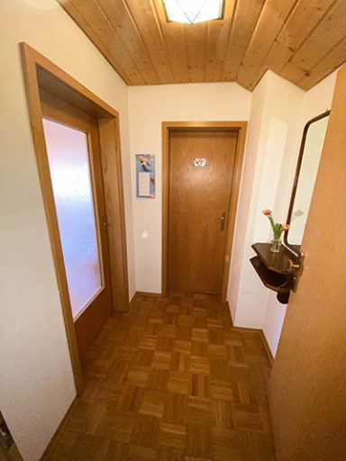 Heller Flur mit Holztüren, einem Wandspiegel und einer kleinen Ablage mit Blumen.