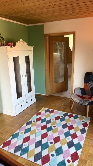Heller Raum mit einer weißen Kommode, einer Tür und einem bunten Teppich in der Villa am Goldbach Bad Aibling.
